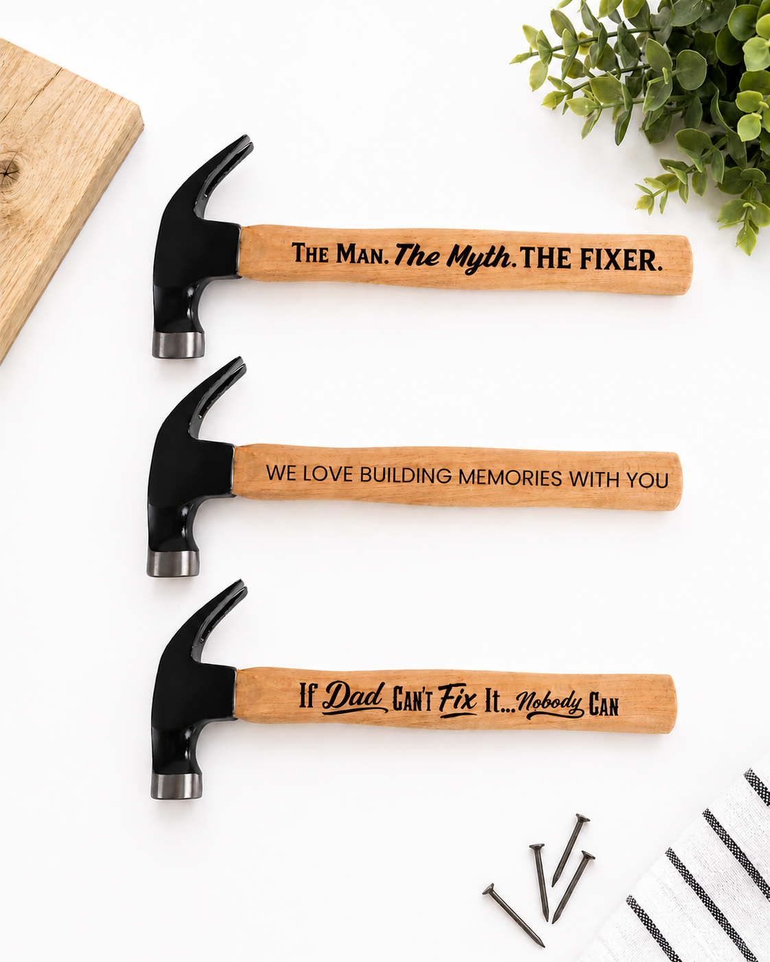 Three hammers with engraved text on a white surface with a plant in the background