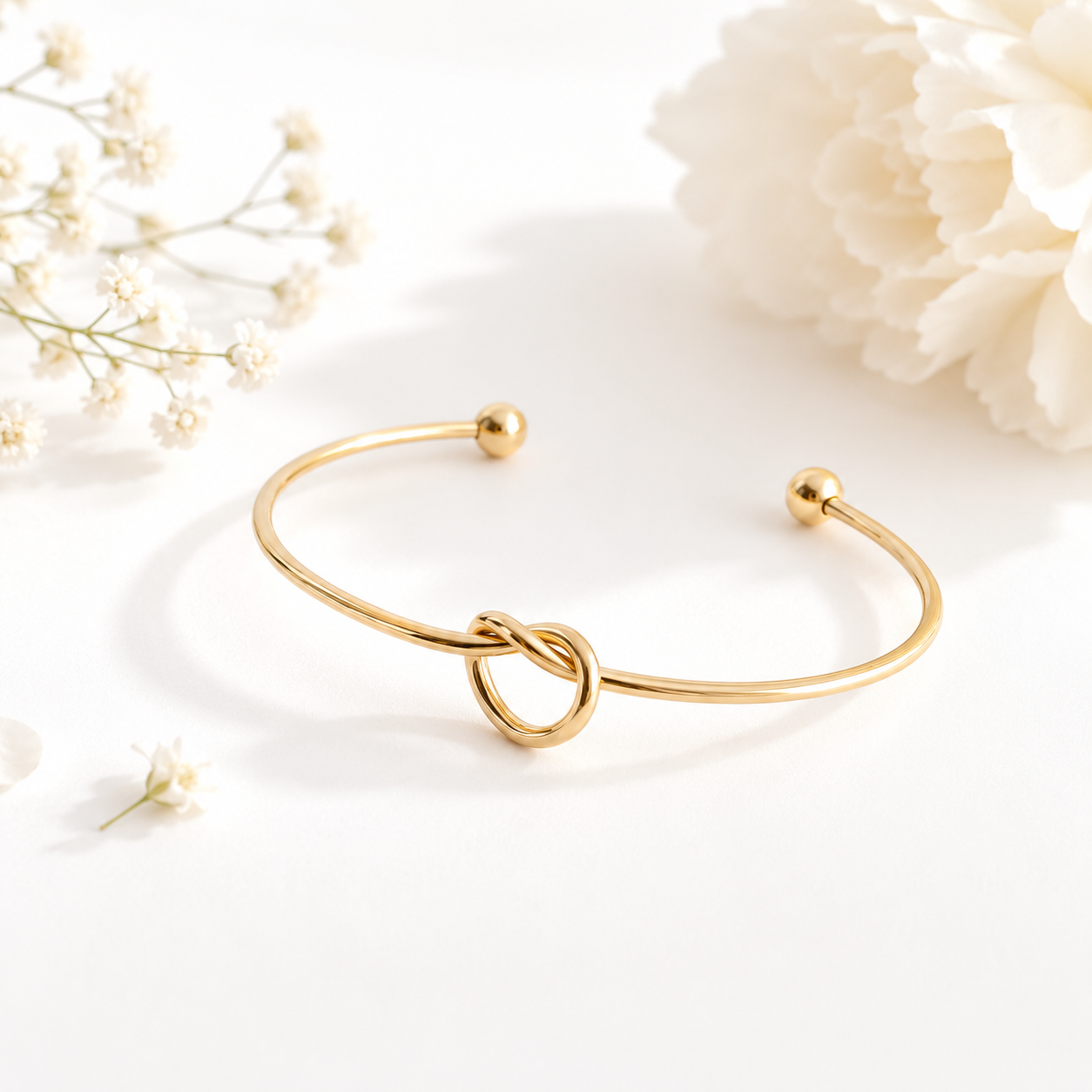 Gold bracelet with a knot design on a white background with flowers