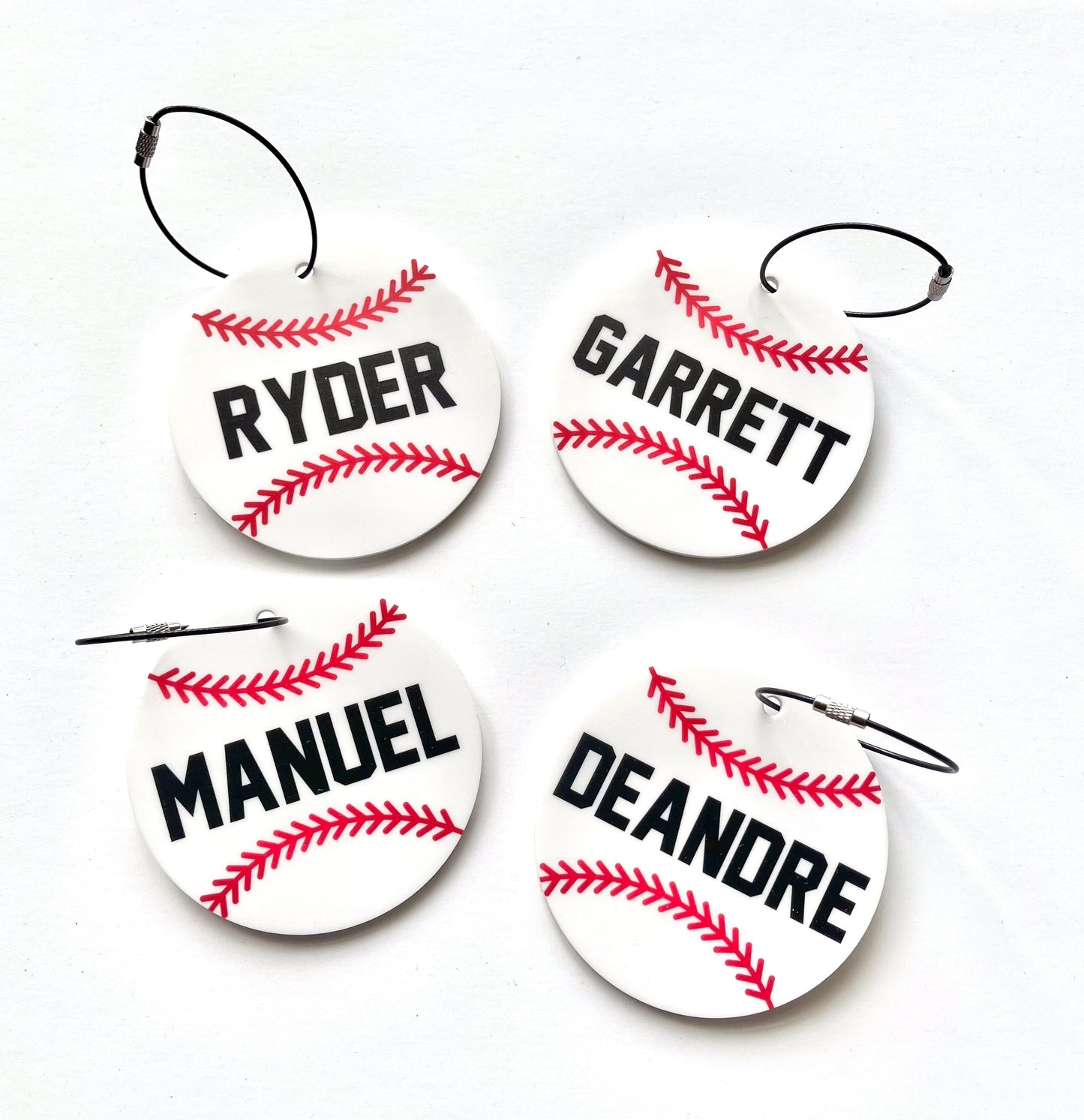 Four baseball keychains bag tags with names printed on them against a white background