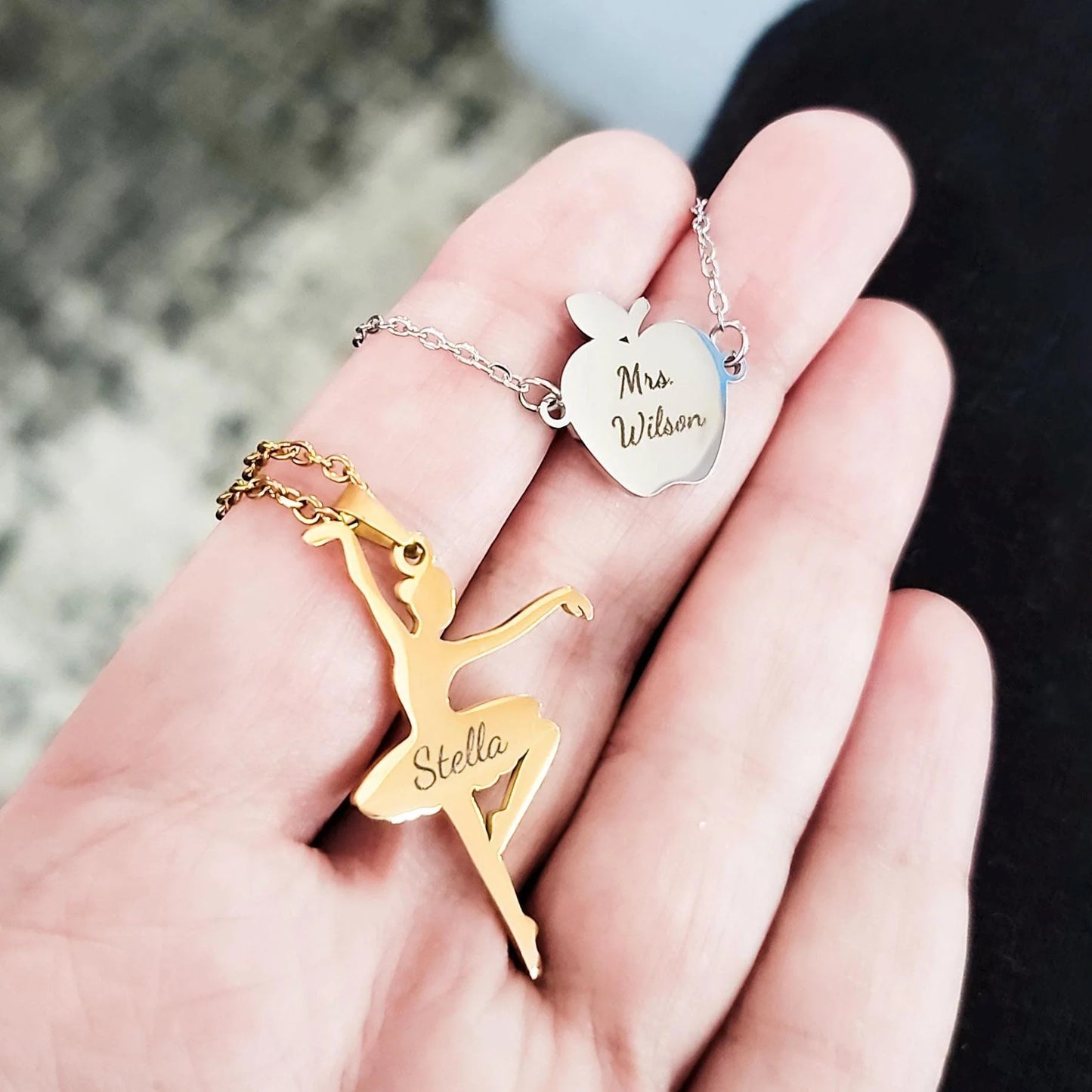 Gold ballerina pendant, silver necklace with 'Mrs Wilson' apple pendant, and blurred background
