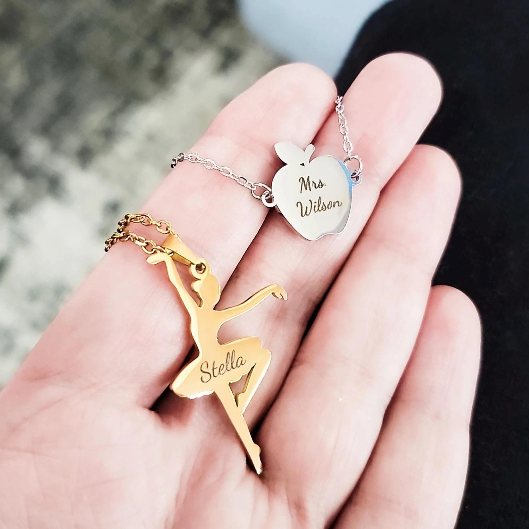 Gold ballerina pendant, silver necklace with 'Mrs Wilson' apple pendant, and blurred background