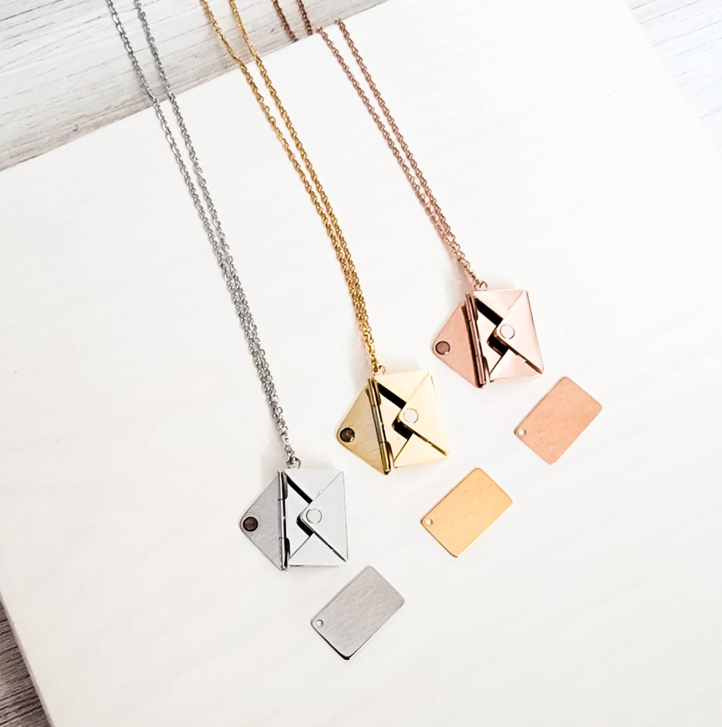 Set of geometric pendant necklaces in silver, gold, and rose gold on a light background.