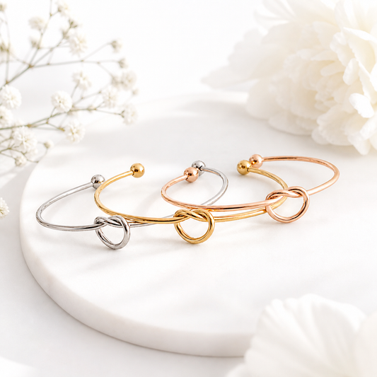 Three gold, silver, and rose gold bracelets on a white surface with flowers in the background.